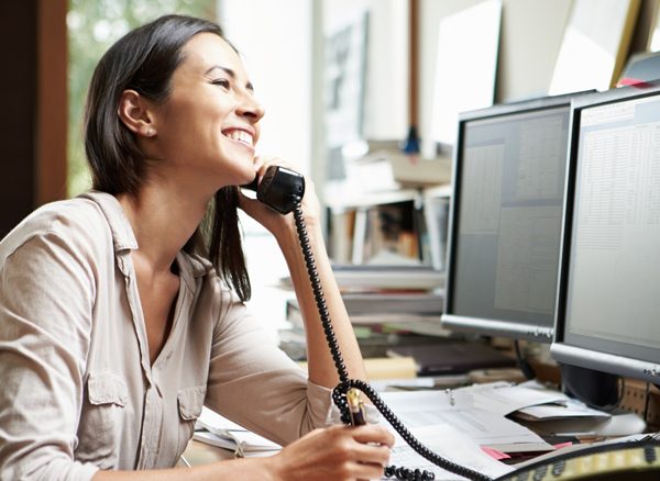 Smiling travel booker at desk on the phone to CTM support