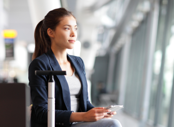 Businesswoman sitting in airport with luggage searching on mobile phone