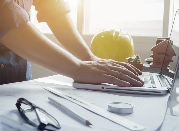 Close up of man's hands working on laptop on table with yellow hard hat behind them