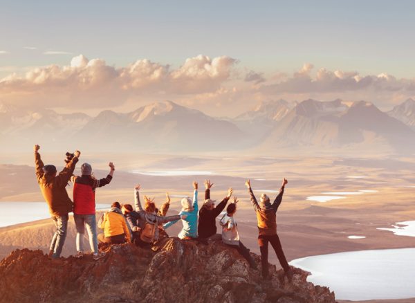 Corporate travelers on incentive trip raising hands on mountain top with mountain ranges in the distance