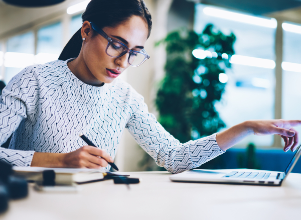 Businesswoman sitting at desk holding pen and working on laptop