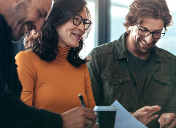 Travel Managers smiling and conversing while male travel manager writes notes with pen