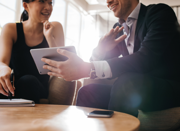 Smiling male travel manager showing smiling female travel manager an iPad